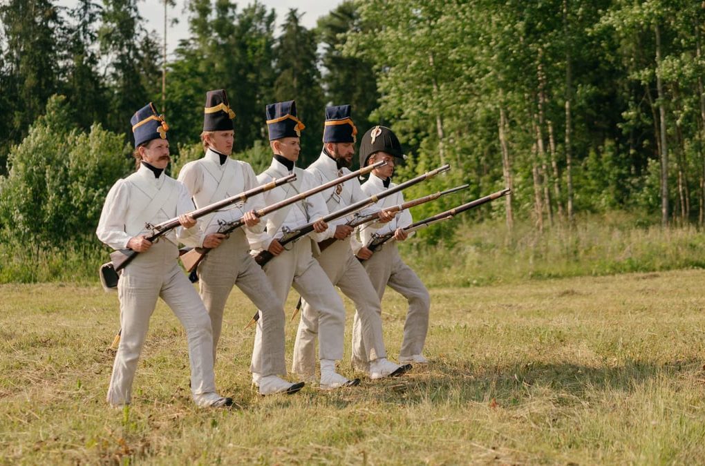 Soldiers in historical uniforms marching during a reenactment in nature.