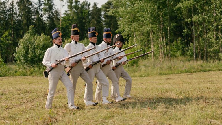Soldiers in historical uniforms marching during a reenactment in nature.
