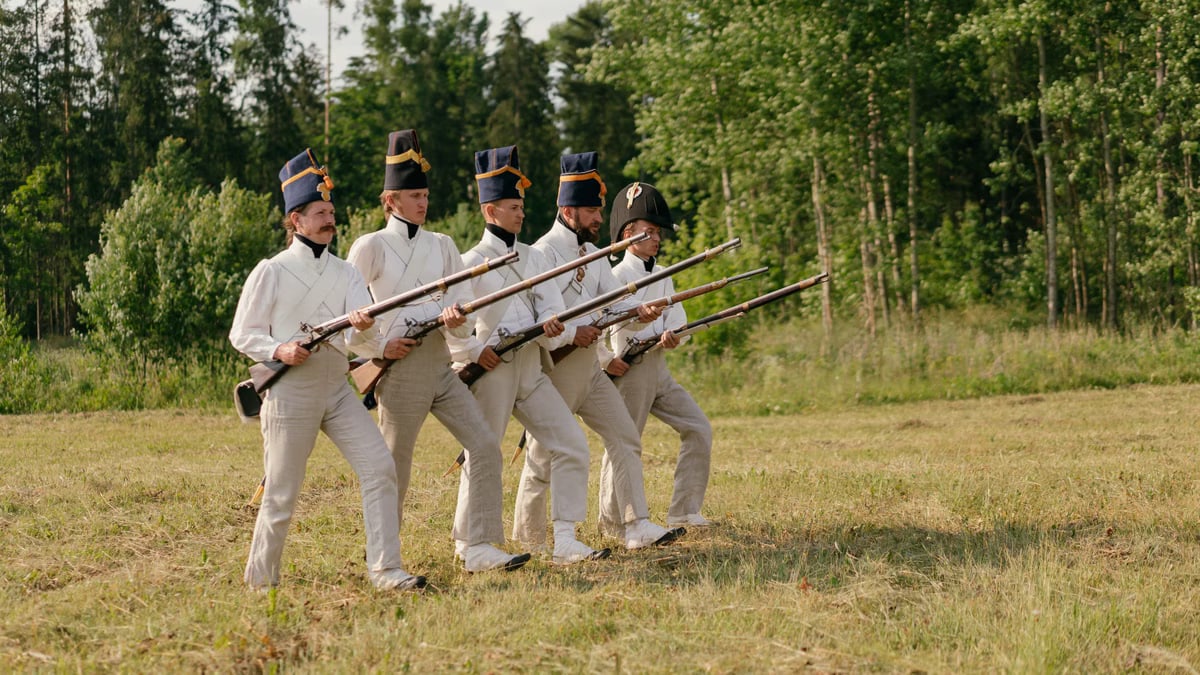 Soldiers in historical uniforms marching during a reenactment in nature.