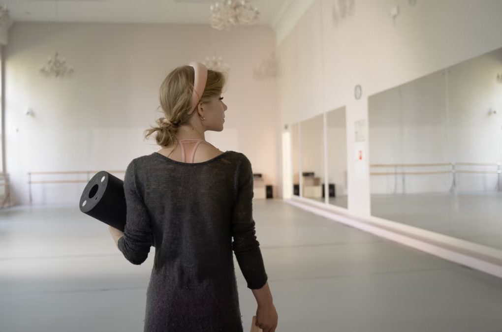 A ballet dancer holds gear in a spacious and elegant studio, ready for practice.
