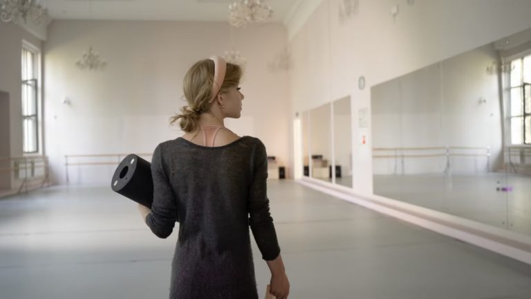 A ballet dancer holds gear in a spacious and elegant studio, ready for practice.